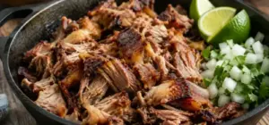Shredded carnitas with crisped edges in a cast iron pan with lime and onion