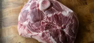Raw bone-in pork butt on a wooden butcher block, showing the muscle groups