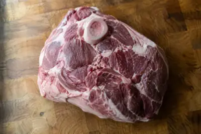Raw bone-in pork butt on a wooden butcher block, showing the muscle groups