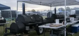Barbecue competition cook site at dawn with offset smokers under a canopy