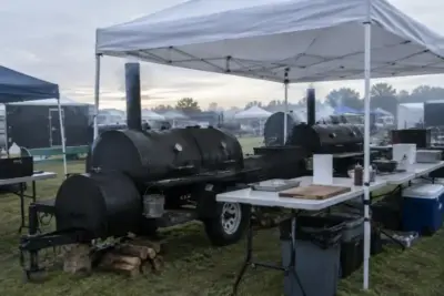 Barbecue competition cook site at dawn with offset smokers under a canopy