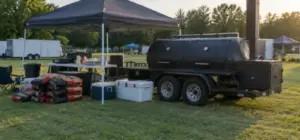 Competition team setup with trailer smoker, canopy, coolers and charcoal