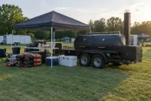 Competition team setup with trailer smoker, canopy, coolers and charcoal