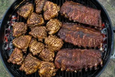 Charcoal grill grate fully loaded with chicken thighs and racks of ribs